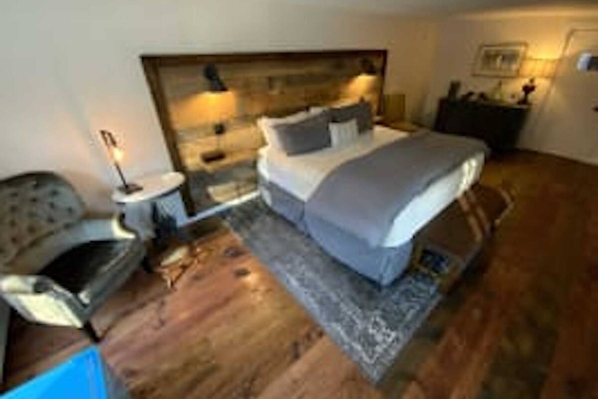 A bedroom with a large bed, a nightstand, a chair, and a wooden headboard.