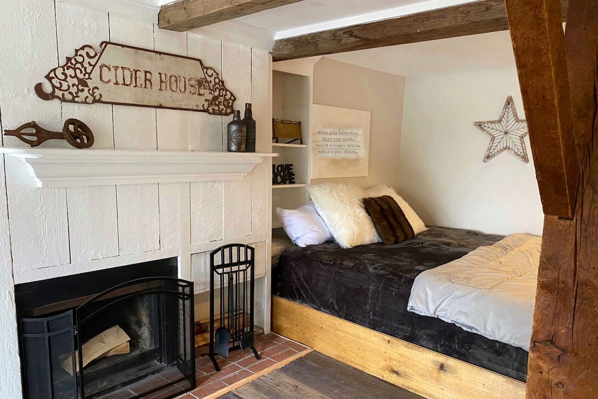 A cozy room with a fireplace, a bed with a headboard, and a sign that reads "CIDER HOUSE".