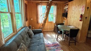A cozy cabin interior with a sofa, dining table, and a ladder leading to a loft. - White Oak Tree House by Garden of the Gods in the Shawnee National Forest (Elizabethtown)