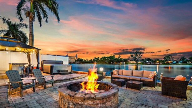 A fire pit surrounded by outdoor seating, a pool, and a sunset view. - NEW! Drift Inn-Lakefront Home w/ Hot Tub, Outdoor Bar, Golf! (Lake Worth)
