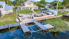A house with a backyard pool, a patio with outdoor furniture, and a dock extending into the water.