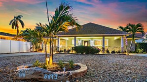 A well-lit residential property with a stone driveway, palm trees, and a flag. - NEW! Drift Inn-Lakefront Home w/ Hot Tub, Outdoor Bar, Golf! (Lake Worth)