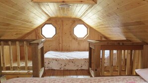 Un dormitorio de buhardilla con techo inclinado, dos ventanas octogonales, una cama con ropa de cama floral y una barandilla de madera alrededor de la cama.
