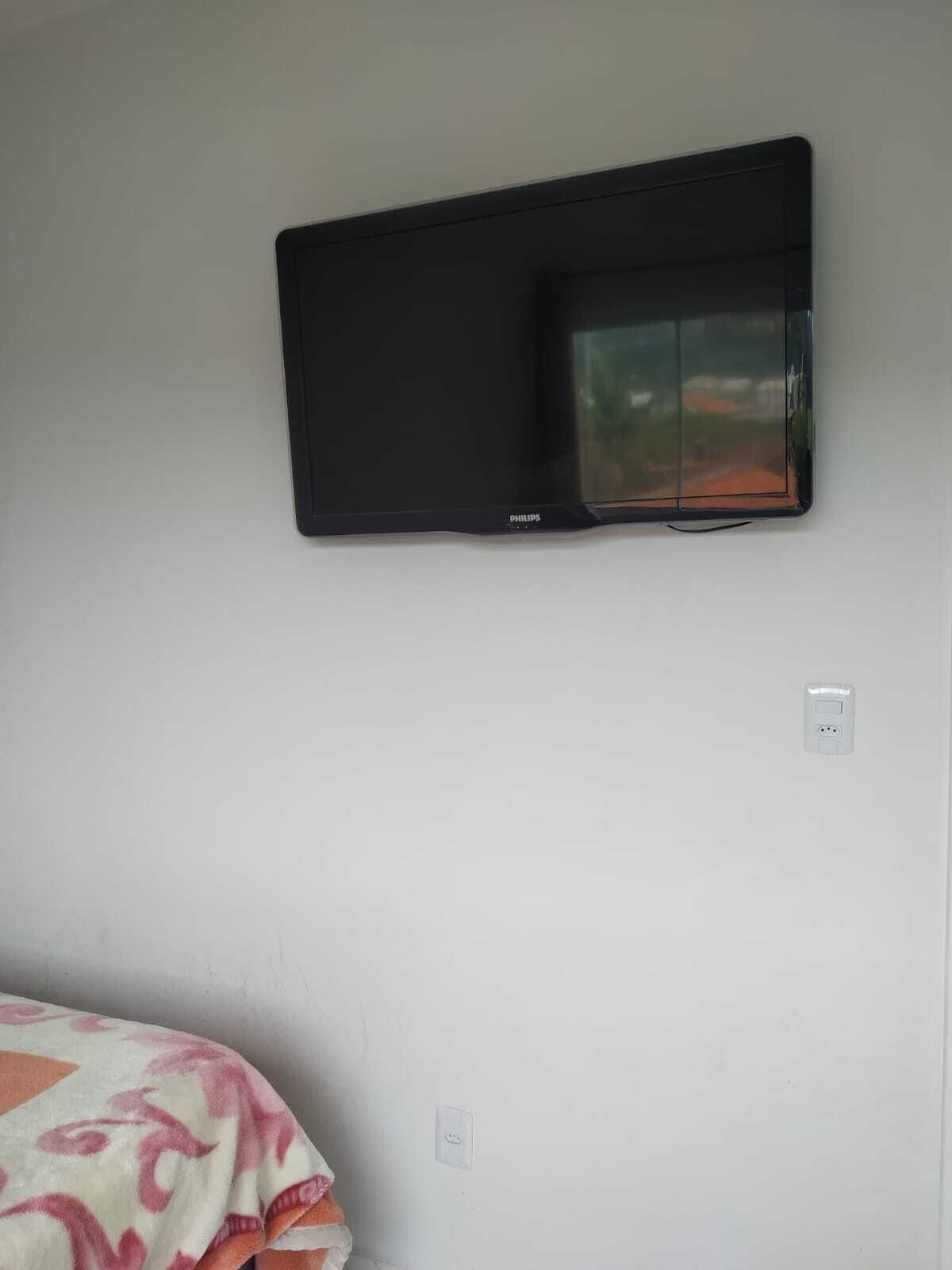 Une chambre dotée d’un téléviseur à écran plat fixé au mur, d’une prise de courant et d’un lit recouvert d’une couverture à motifs.
