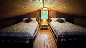 Une chambre mansardée chaleureuse, avec deux lits, une petite table et une fenêtre.