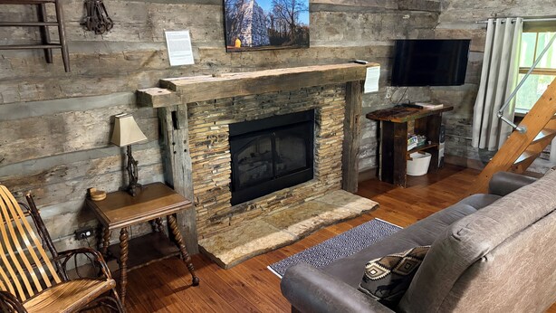 Un salon rustique avec une cheminée en pierre, des meubles en bois, un téléviseur et un tableau accroché au mur.
