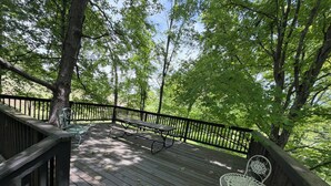 Une terrasse en bois avec une table de pique-nique et des chaises, entourée d’arbres.