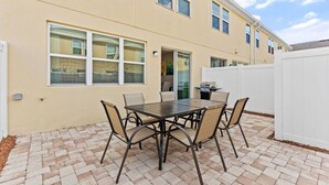 A patio with a table and chairs, a white fence, and a building with windows. - 5129 Compass Bay 8 guests 4DBR BBQ near Disney (Kissimmee)
