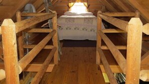 A wooden attic bedroom with a bed, a window with curtains, and a wooden ladder. - The Hickory Hollow Log Cabin by Garden of Gods in the Shawnee National Forest (Elizabethtown)