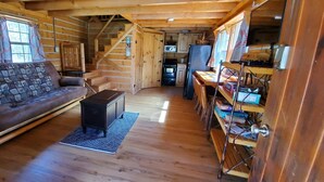 Un interior de cabaña acogedor con un sofá, una pequeña mesa, una escalera y una zona de cocina.