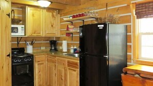 Cocina de cabaña de madera con refrigerador, estufa y microondas negros.