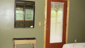 A room with a wooden bench, a door with a window, and a bed with a floral bedspread. - The Pine Ridge Home by Garden of the Gods in the Shawnee National Forest (Herod)