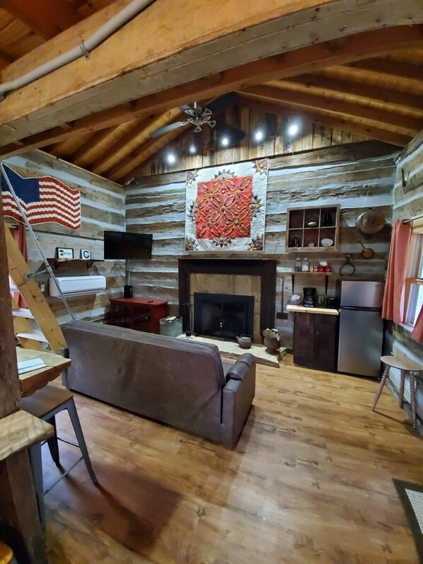 A log cabin interior with a fireplace, wooden floors, a sofa, and a television.