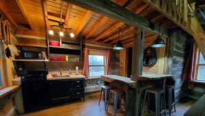 A rustic kitchen with wooden beams, a stove, a sink, and bar stools.