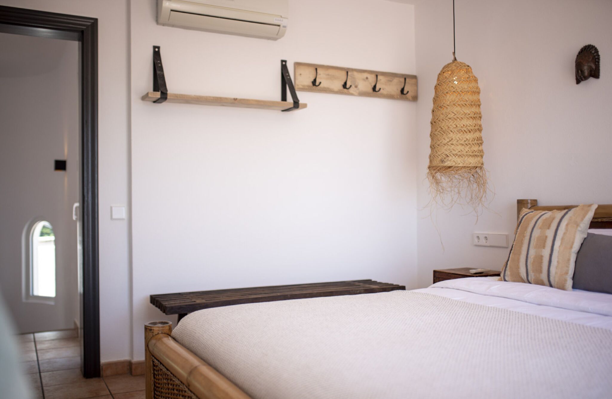 A bedroom with a bed, a bedside table, a wall-mounted shelf with hooks, and a hanging light fixture.