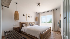 Een slaapkamer met een houten bed, een bankje, een hanglamp en uitzicht op het omliggende landschap.
