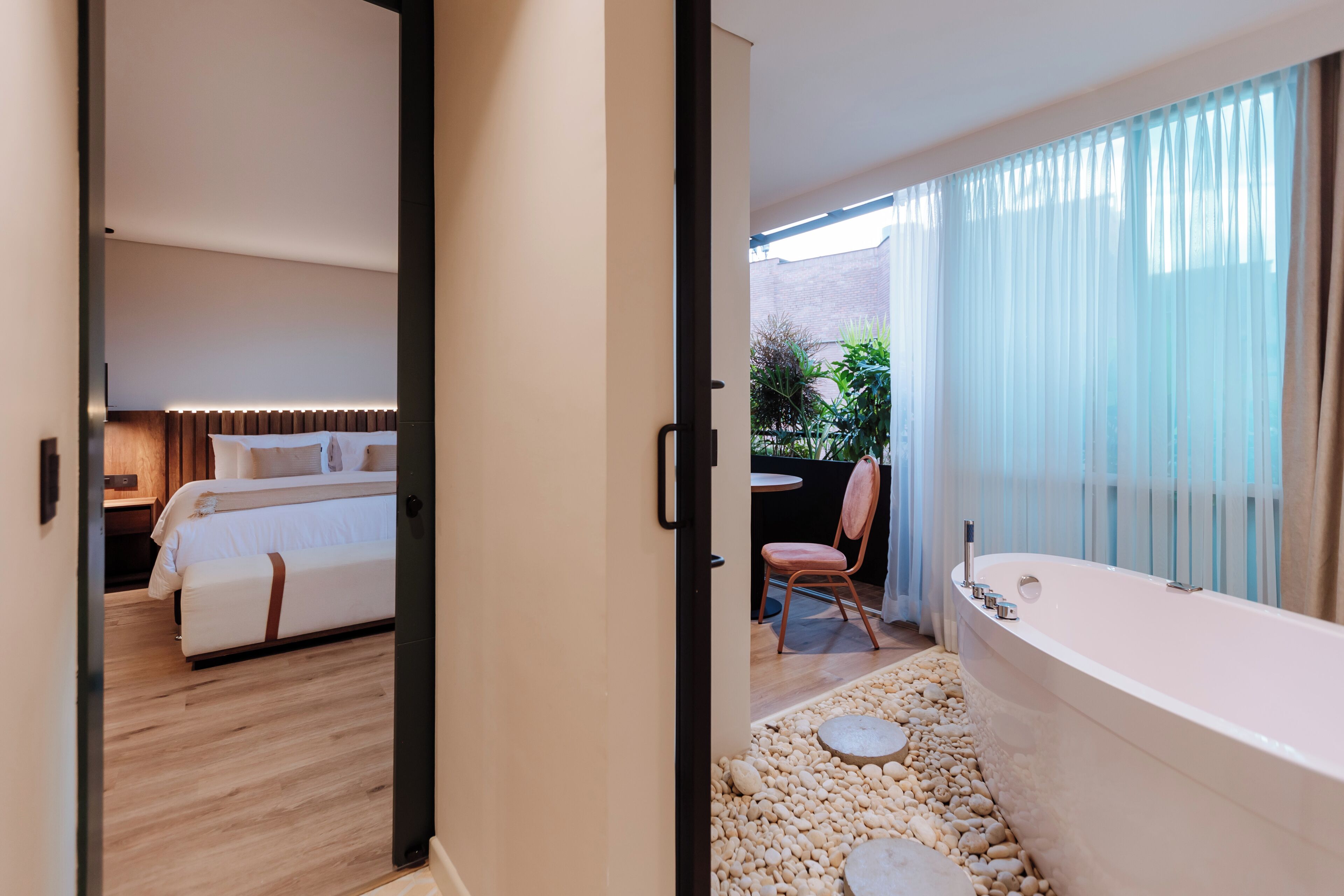Een moderne hotelkamer met een bed, een badkamer met bad en een zithoek met een stoel en tafel.