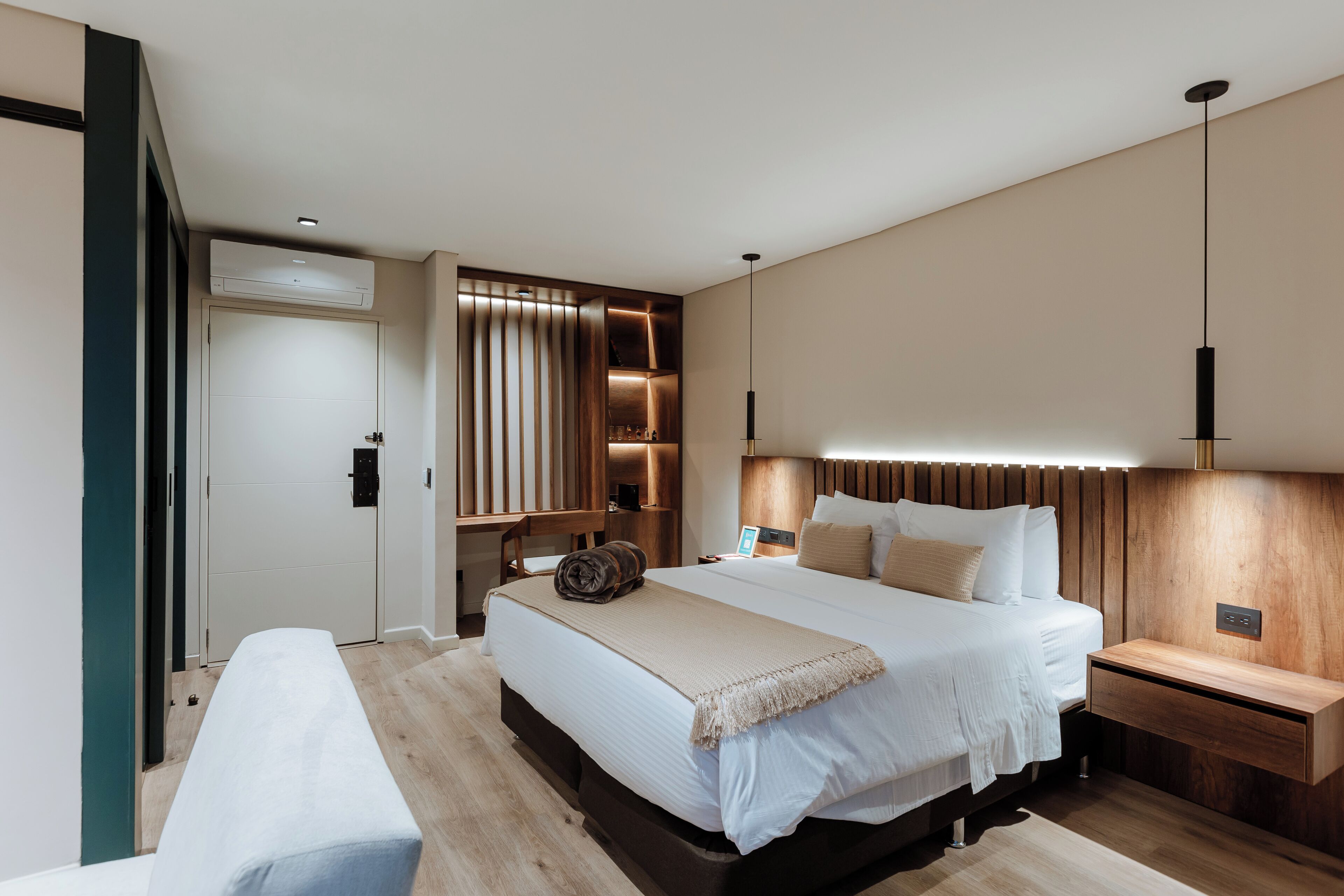 Un dormitorio moderno con una cama grande, mesitas de noche, un banco y estanterías empotradas.