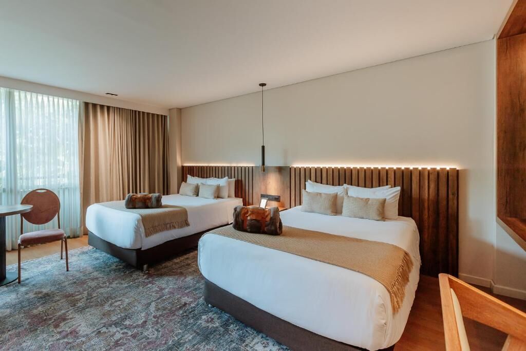 Une chambre d’hôtel avec deux lits, un bureau, une chaise et une grande fenêtre avec des rideaux.