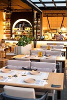 Un restaurant avec des tables dressées pour le service, un bar et un espace salon avec des fauteuils confortables.