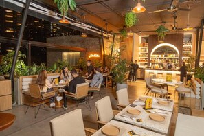 Un comedor interior con mesas dispuestas para comidas, rodeado de plantas y follaje colgante.