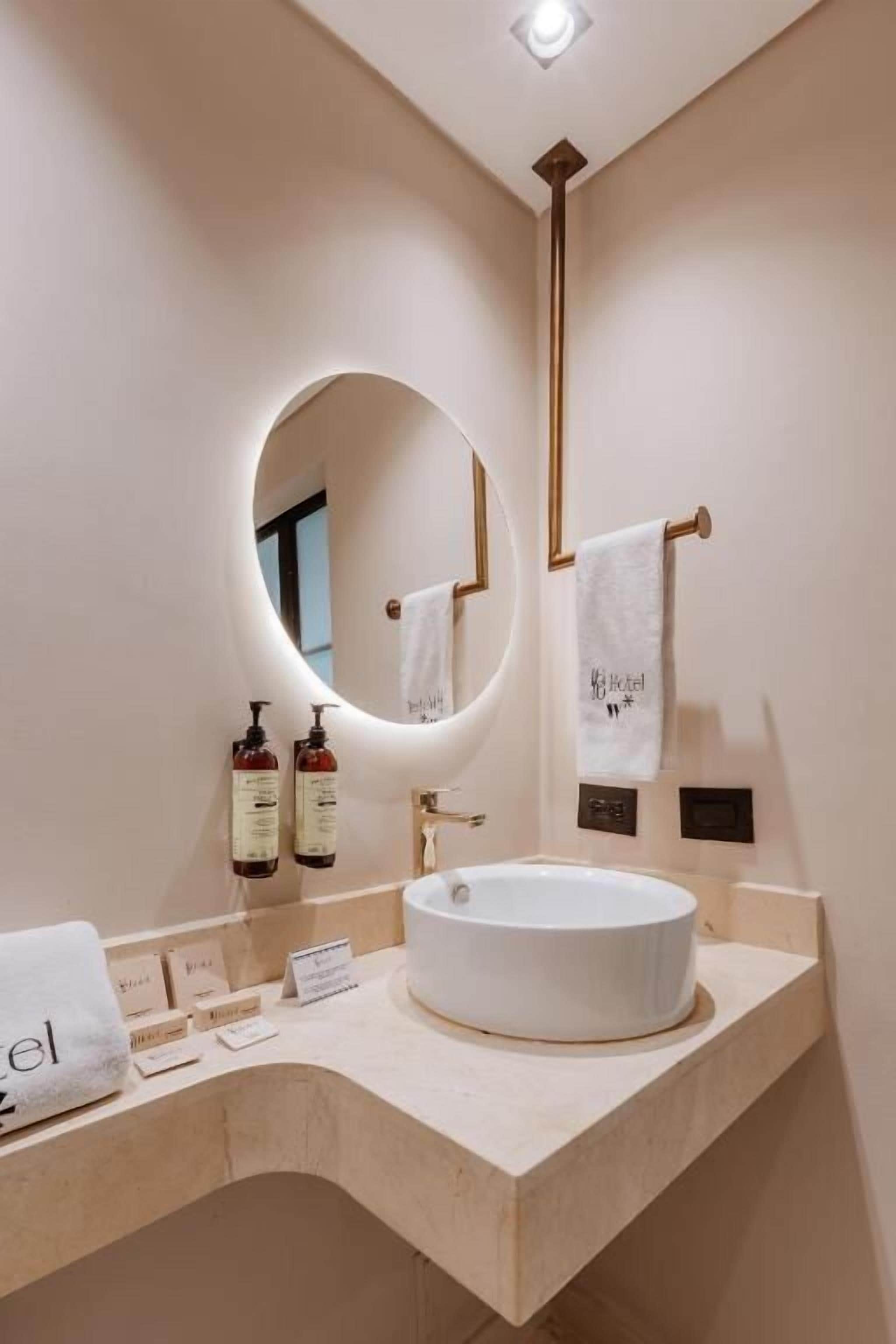Een moderne badkamer met een ronde spiegel, een witte wastafel en een handdoekrek.