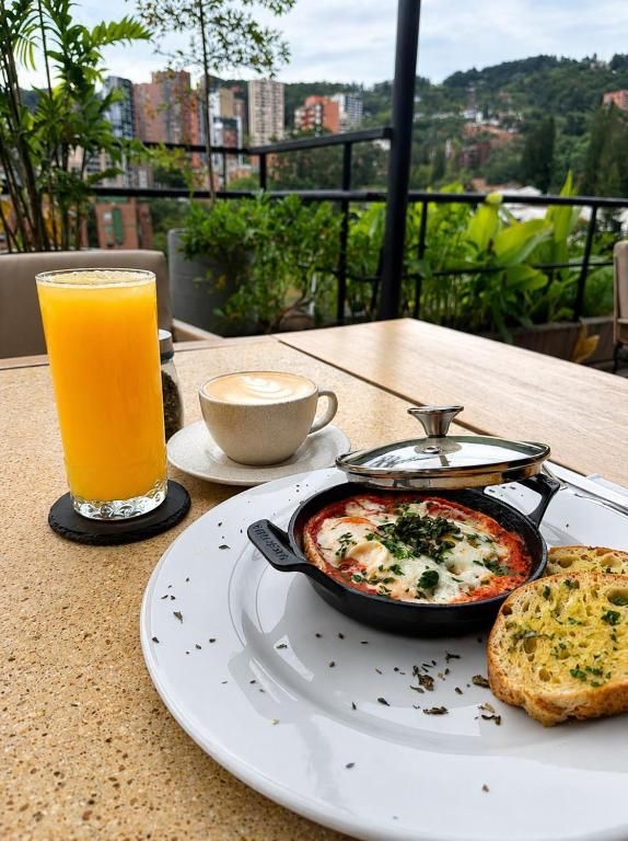 A table with a breakfast setting including a glass of orange juice, a cup of coffee, a dish with cheese and herbs, and a slice of bread.