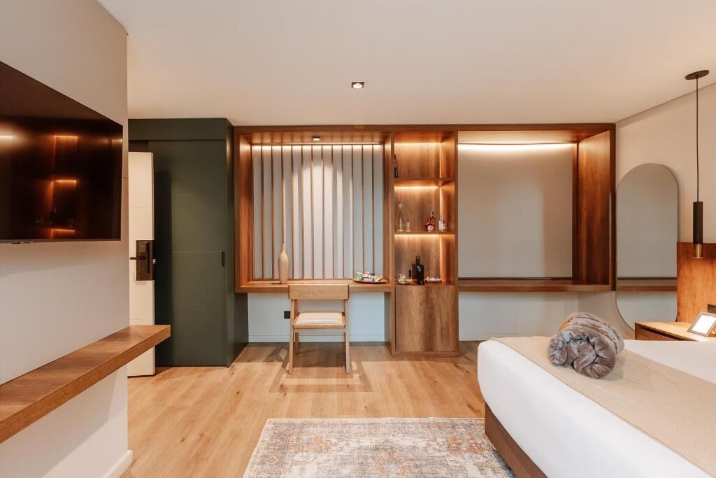 Una habitación de hotel moderna con un escritorio de madera, una cama, un televisor y un estante empotrado con objetos decorativos.