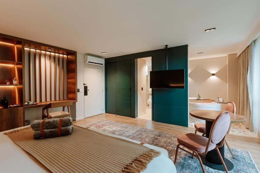 Ein modernes Hotelzimmer mit einem Bett, einer Sitzecke mit Tisch und Stühlen, einem Flachbildfernseher und einem durch eine offene Tür einsehbaren Badezimmer.