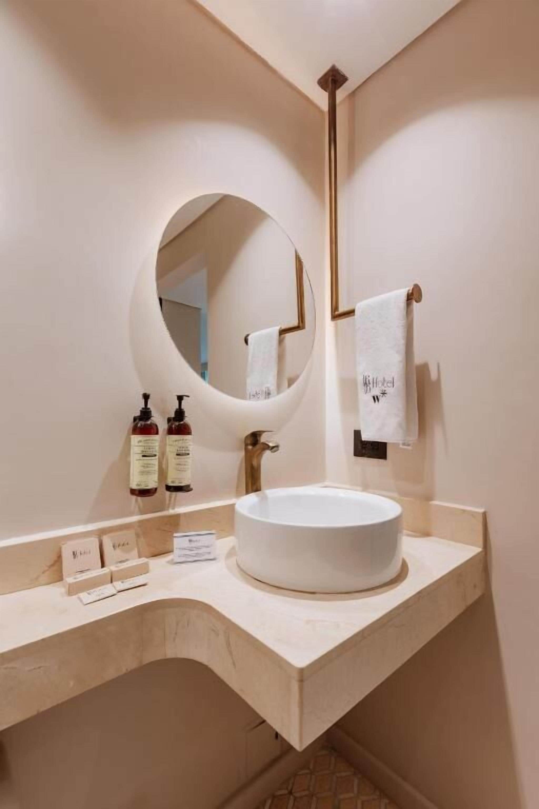 A bathroom with a round mirror, a white sink, and two bottles of shampoo.