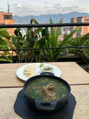 A dining table with a bowl of soup and a plate of flatbreads, set against a backdrop of mountains and buildings. - 1616 HOTEL  (Medellín)