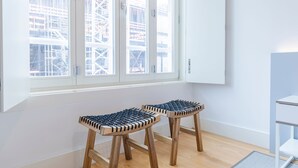 Een kamer met twee houten krukken met zwarte zittingen, een wit kastje en een raam met uitzicht op een bouwplaats.