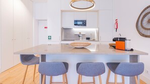 Een moderne keuken met een centraal eiland, barstoelen, een magnetron en een koffieapparaat.