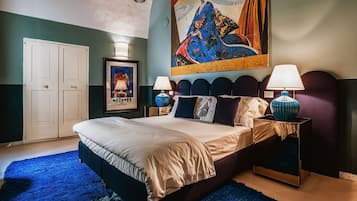 Quarto com uma cama grande, duas mesas de cabeceira com abajures, um guarda-roupa e um quadro colorido na parede.