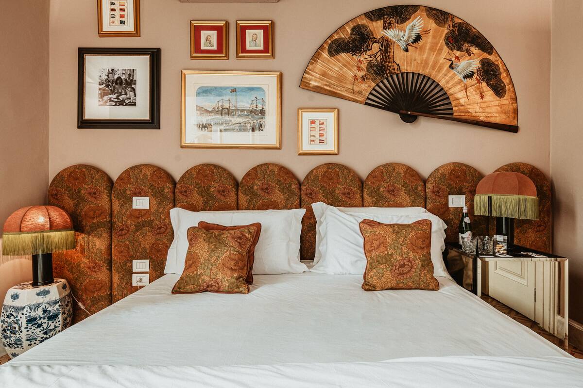 A neatly arranged hotel room with a large bed, a headboard with a unique design, and various framed pictures on the wall.