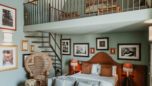A bedroom with a large bed, a sofa, a chair, and a staircase leading to an upper level. - Palazzo Flora (Gallipoli)