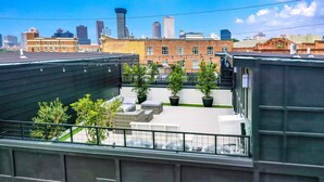 Une terrasse sur le toit agrémentée de plantes en pot, avec des sièges d’extérieur et une vue panoramique sur la ville.