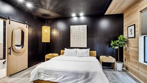 Une chambre moderne avec un grand lit, une tête de lit en bois, un luminaire suspendu, une petite table de chevet et une plante en pot.