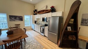 Una cocina moderna con armarios blancos, electrodomésticos de acero inoxidable y una zona de comedor con una mesa y sillas de madera.