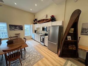 Une cuisine moderne avec des meubles blancs, des appareils en acier inoxydable et un coin repas comprenant une table et des chaises en bois.