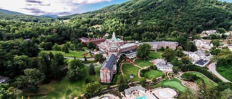 An aerial view of a resort with a large swimming pool, multiple buildings, and lush greenery.