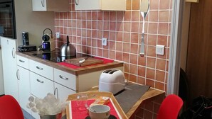 Eine kompakte Küche mit weißen Schränken, einer roten Fliesenwand und einer kleinen Essecke mit zwei roten Stühlen.