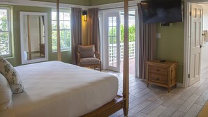 Un lit à baldaquin, une chaise en bois, un téléviseur et une petite armoire en bois dans une pièce aux murs verts et au plancher en bois.