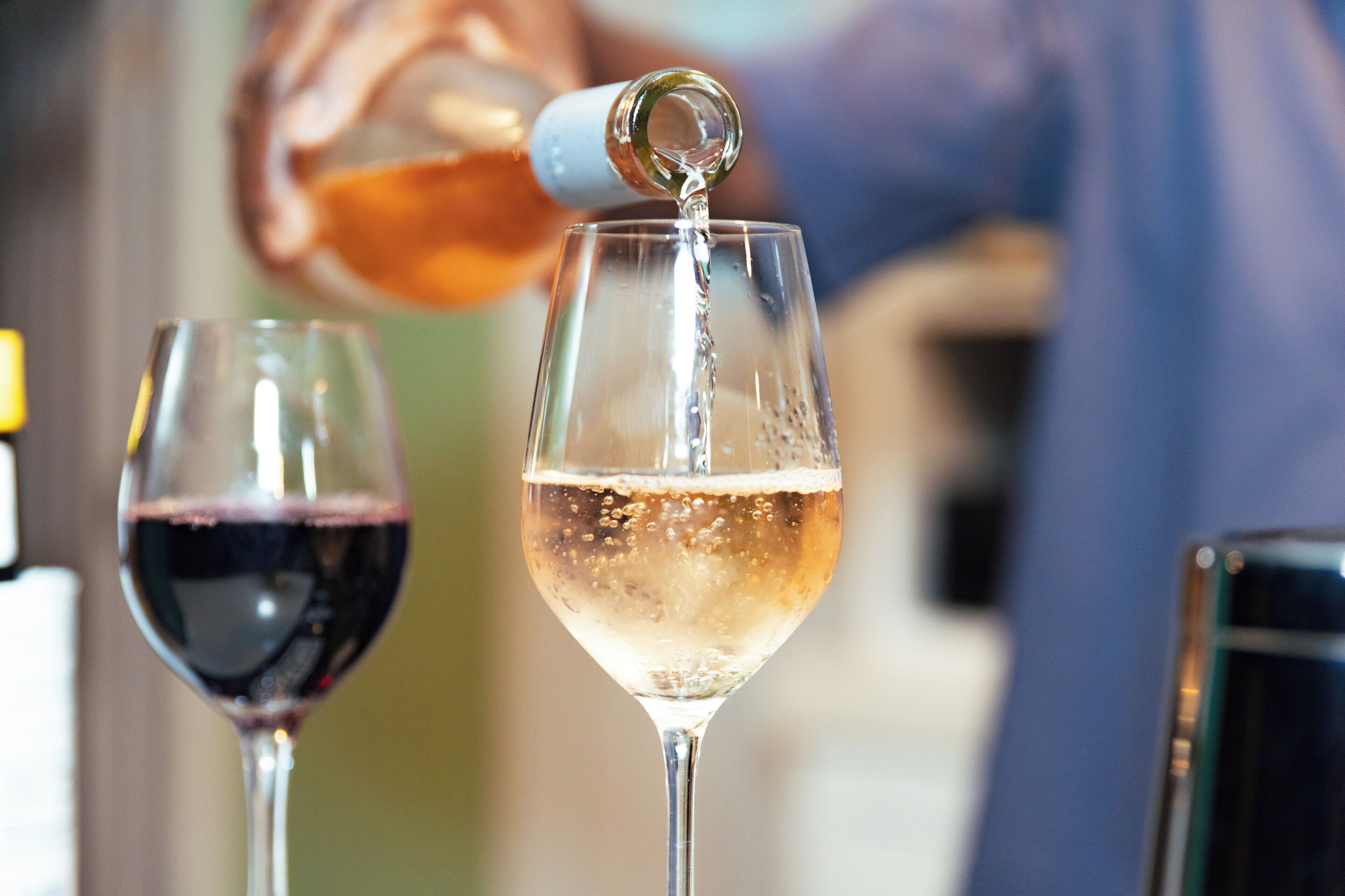 A glass of white wine with bubbles, a glass of red wine, and a bottle pouring into the glass.