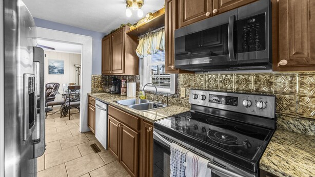 Una cocina con armarios de madera, un refrigerador de acero inoxidable, un microondas, una estufa y un lavamanos.
