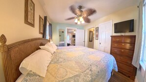 Un dormitorio con cama, cómoda, ventilador de techo y televisor montado en la pared.