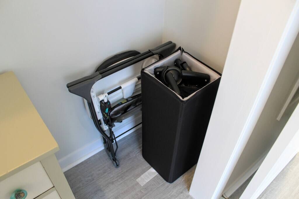 A compact room with a small desk, a black trash bin, and a white wall.