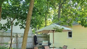 Un patio al aire libre con una mesa, sillas, una parrilla y una sombrilla.