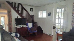Una sala de estar con una escalera, televisor, sofá y lámpara.