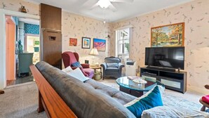 Un salon comprenant un canapé, des fauteuils, une table basse, un téléviseur et un ventilateur de plafond.